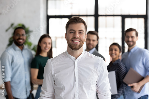 Smiling millennial student looking at camera posing for portrait in front of diverse young people group getting education at international university, happy ambitious intern receiving job at company