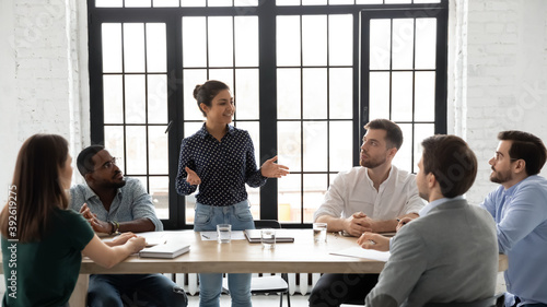 Business coaching. Friendly indian female coach delivering training to diverse group of young employees, capable millennial mixed race woman tutor explaining sales strategy to multiethnic intern team