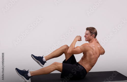 Happy young guy with muscular body working out on sports mat over light studio background