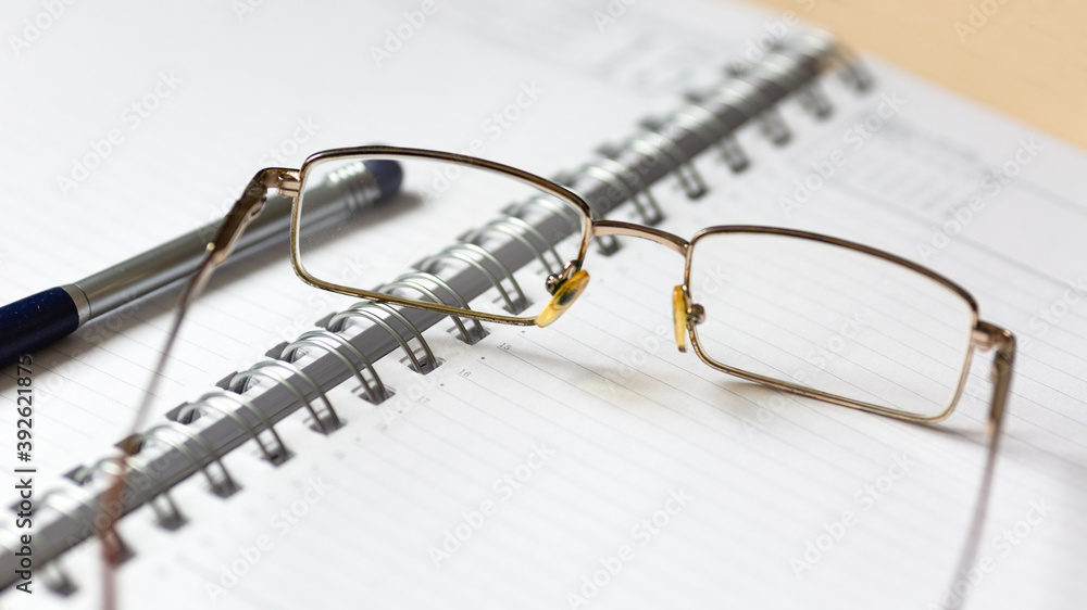 Glasses and a pen on an open notebook. Glasses and a pen on an open notebook.