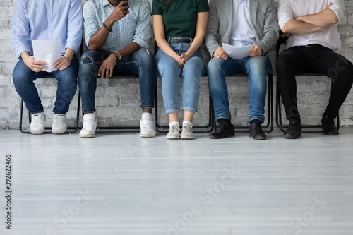 Close up cropped shot of multiethnic group of young job applicants sitting in row at corporate office corridor preparing waiting for interview with hr feeling worry calm confident patient, copy space