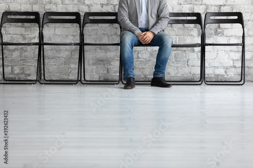 I might be next. Cropped shot of young male patient expecting for doctor appointment, confident unemployed specialist sitting on chair in empty row in calm pose waiting for meeting with hr, copyspace photo