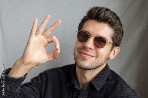 Portrait of a young attractive guy in a glasses with a beautiful smile showing an OK sign isolated 