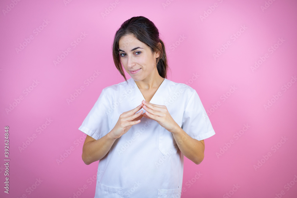 Young brunette doctor girl wearing nurse or surgeon uniform over isolated pink background with Hands together and fingers crossed smiling relaxed and cheerful. Success and optimistic Young brunette doctor girl wearing nurse or surgeon uniform over isolated pink background with Hands together and fingers crossed smiling relaxed and cheerful. Success and optimistic
