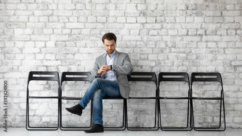 Time is money. Serious young businessman job applicant sitting at company office employment agency hall expecting for interview looking at wrist watch checking time thinking he is waiting too long