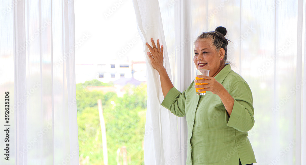 Senior Asian women I was drinking orange juice while standing by the window in the background of the room. Senior Asian women I was drinking orange juice while standing by the window in the background of the room.