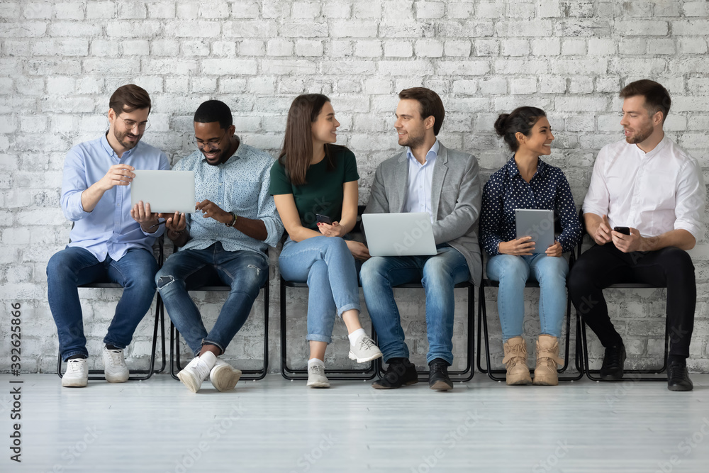 Fototapeta premium Sharing information. Diverse young people of millennial generation sitting in line talking chatting communicating using electronic devices sharing data discussing apps software new models of gadgets