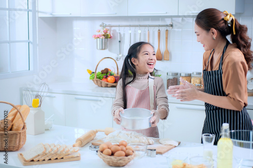 Happy Asian mother and adorable daughter helping knead the dough to make a bakery in the kitchen.