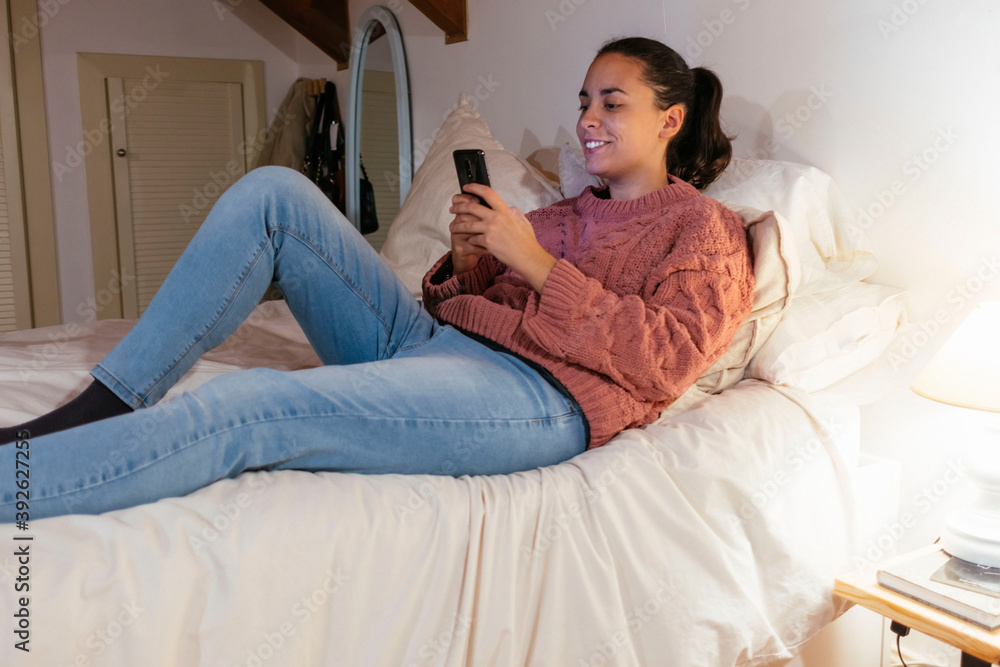 Young woman using a mobile lying on her bed. Relax time. Young woman using a mobile lying on her bed. Relax time.