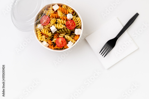 Pasta with tomato and feta in taking away box on white table