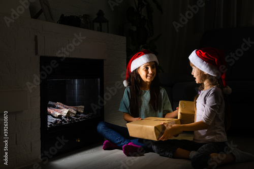 two little girls sitting by a fireplace in a cozy dark living room on Christmas eve