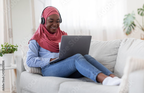Enjoying time at home. Black muslim woman using laptop and drinking coffee