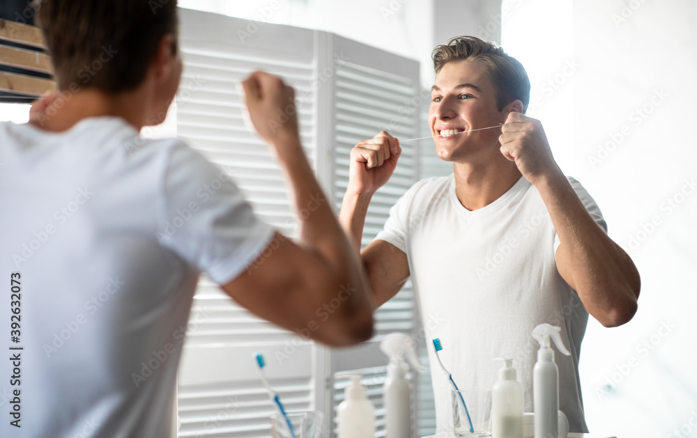 Young guy using his dental floss in bathroom Young guy using his dental floss in bathroom