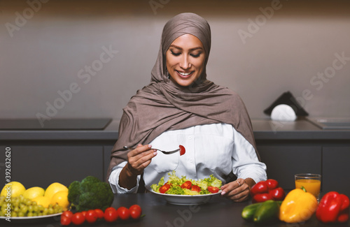 Muslim Lady Eating Vegetable Salad For Dinner In Modern Kitchen