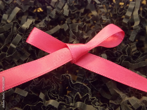 Pink ribbon out of fabric on black paper shreds 