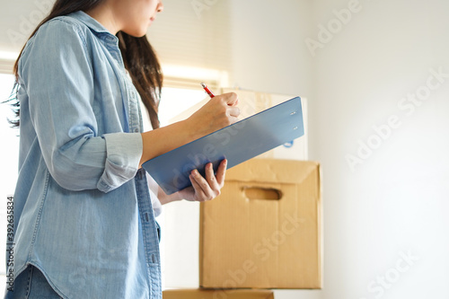 Asian woman checking and packing carton boxes prepare to move to new house relocation shipping or check goods package before delivery to customer by checklist photo