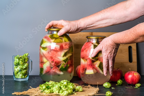 Woman pickles watermelon with apples and hops in a glass jar on a wooden table