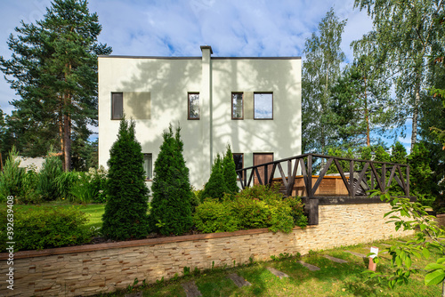 Modern exterior of private cottage. Garden with thujas and flowers. Green lawn. Decorative stone flowerbed. © Aleks Kend