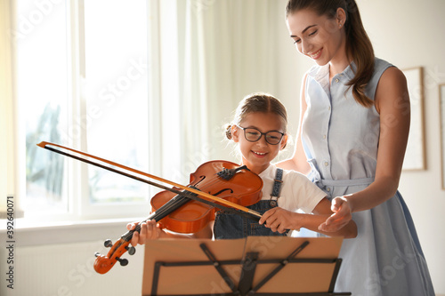Canvas Print Young woman teaching little girl to play violin indoors