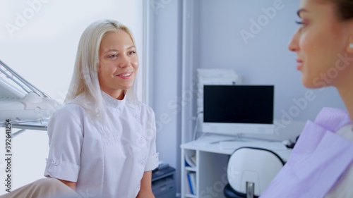 Professional Blonde Happy Female Dentist  Discussion Of The Treatment Plan And Healthy Smile With Patient. Concept Of Clean And Healthy Teeth