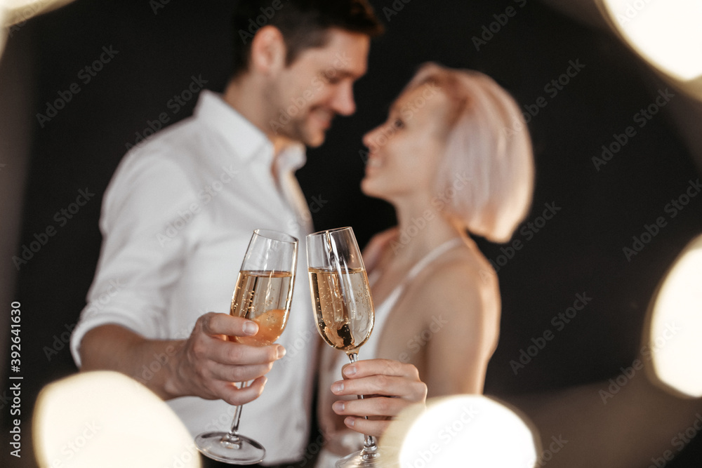 Beautiful happy couple young family in evening dresses with glasses of champagne on the dark background, selective focus