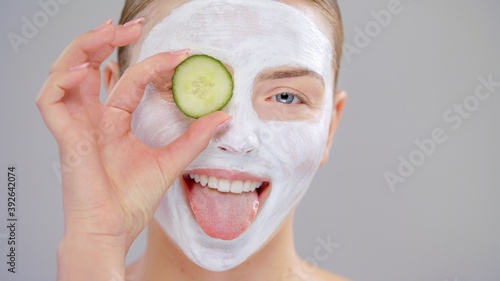 Extreme Closeup Portrait Young Caucasian Beautiful Blonde Woman With Blue Eyes She Covering Eye Fresh Cucumber White Mask Cosmetic On Face And Smiling On Gray Background Skin Care Concept