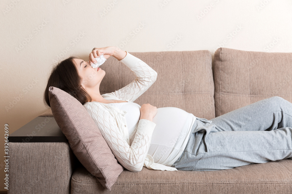 Sick pregnant woman blowing nose into tissue at home Healthy millennial healthcare concept Sick pregnant woman blowing nose into tissue at home Healthy millennial healthcare concept