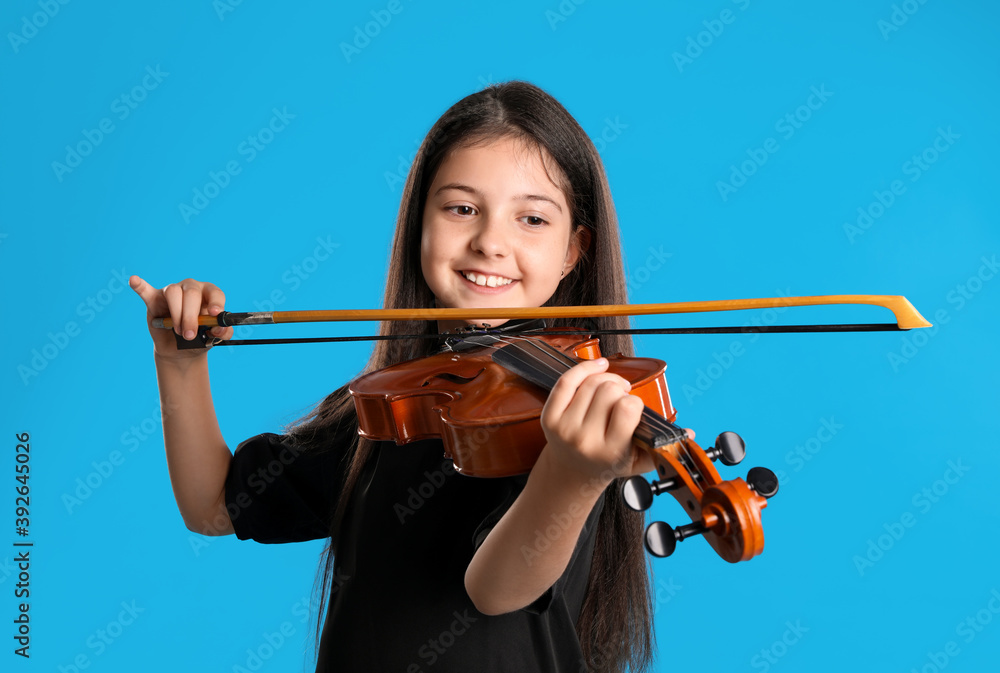 Preteen girl playing violin on light blue background Preteen girl playing violin on light blue background