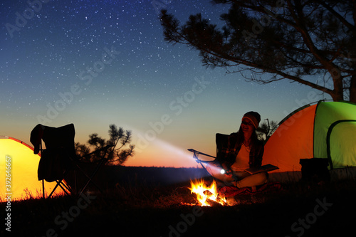 Woman with flashlight near bonfire at night. Camping season