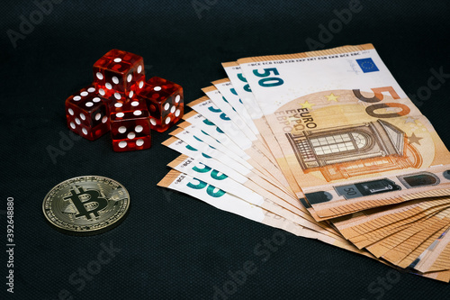 Bitcoin coin, a pile of Euro banknotes and a few red cubes lie side by side on a dark background photo