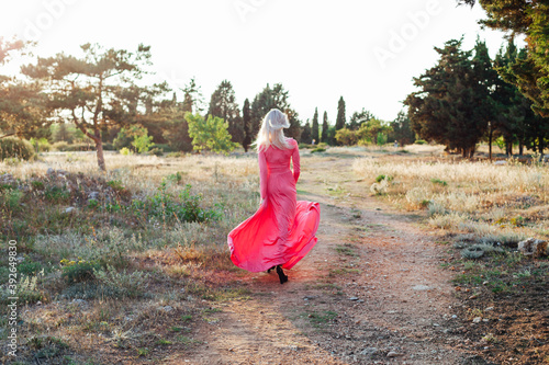 Beautiful blonde woman in pink dress walks in the park at sunset