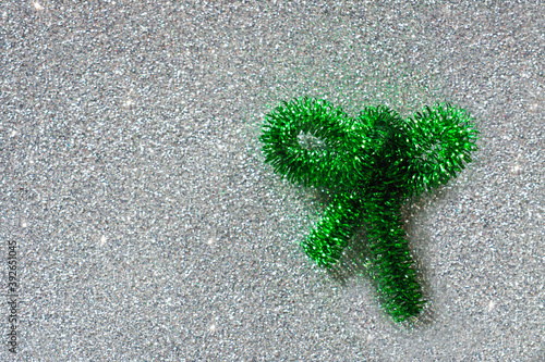 Green bow made of festive garland on shiny silver background, copy space