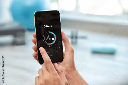 Young woman using fitness app on smartphone indoors, closeup