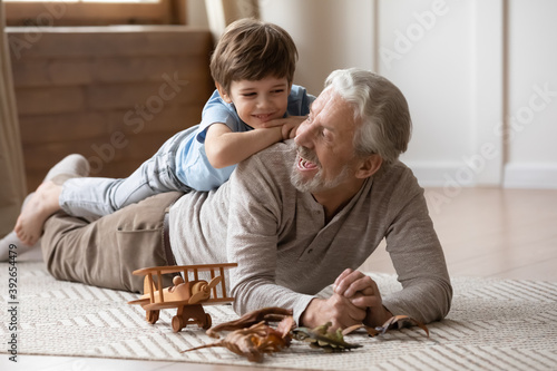 Fotografia Overjoyed mature grandfather playing with adorable grandson at home, older man l