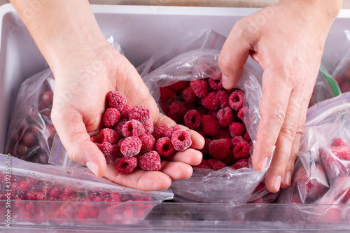 Fototapeta Naklejka Na Ścianę i Meble -  Frozen raspberry in hand, closeup. Frozen berries and fruits in a plastic bag in refrigerator