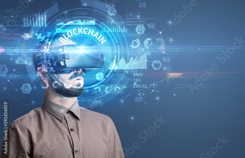 Businessman looking through Virtual Reality glasses with BLOCKCHAIN inscription, innovative technology concept
