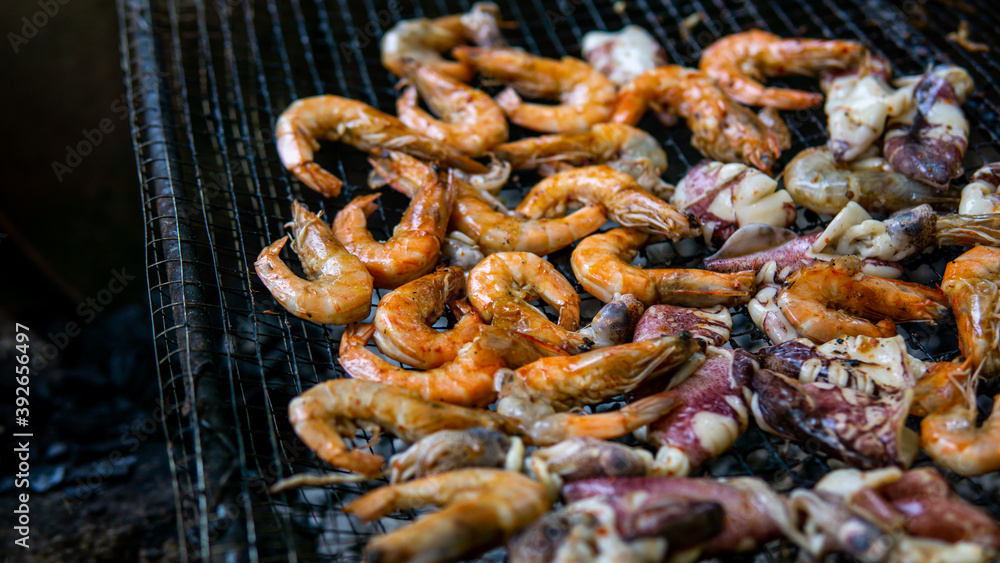 Close up view of grilled prawns and squids on the hot grill during summer picnic. Roasted seafood menu on a charcoal stove. Selective focus.