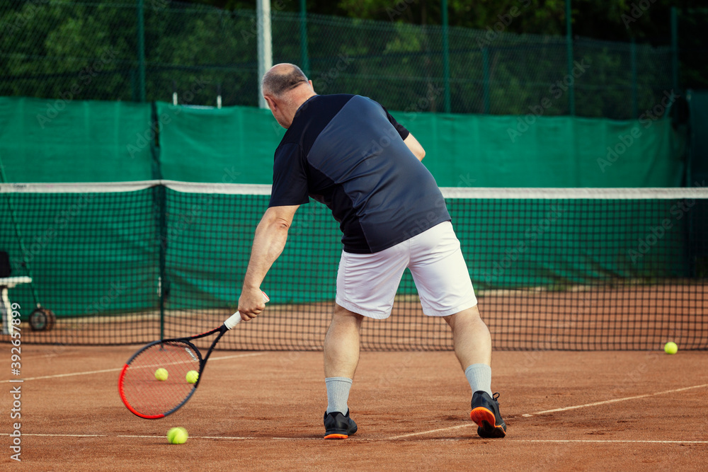 An aged man plays tennis on the court. Active lifestyle and health. Back view.