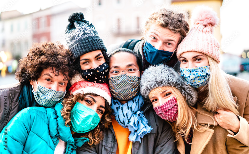 Multiracial friends taking selfie wearing face mask and winter clothes - New normal lifestyle concept with young people having fun together outside - Bright filter with focus on central asian guy - obrazy, fototapety, plakaty 