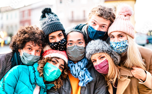 Multiracial friends taking selfie wearing face mask and winter clothes - New normal lifestyle concept with young people having fun together outside - Bright filter with focus on central asian guy