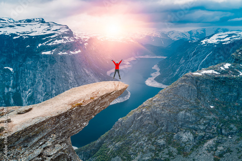 Norway, A woman Jumping on the mountains cliff edge of Trolltunga throning over Ringedalsvatnet  watching the sunset and snowy Norwegian mountains near Odda, Rogaland, Norway photo