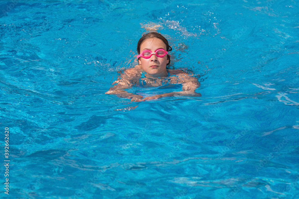Girl in glasses swim in the blue swimming pool.