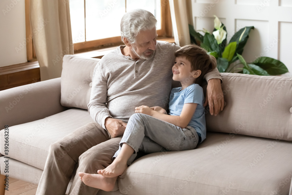 Mature grandfather talking with adorable grandson, sitting on couch, loving old man and little boy grandchild enjoying leisure time, tender moment, having pleasant conversation, two generations Mature grandfather talking with adorable grandson, sitting on couch, loving old man and little boy grandchild enjoying leisure time, tender moment, having pleasant conversation, two generations