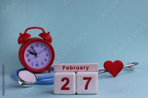 February 27st. White wooden calendar blocks with date, clock and stethoscope on blue pastel background. Selective focus. health concept photo