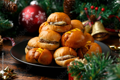 Christmas mini hamburgers, burger and hot dogs with decoration, gifts, green tree branch on wooden rustic table
