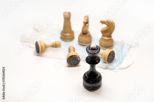 wooden chess pieces on a medical mask. Black's Queen is watching