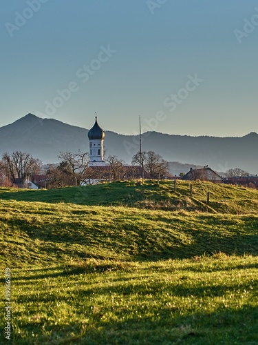Bell tower on green hills in the alps during sunset. Church in front of a mountain silhouette during sunset. Church on green hills in the mountains during sunset.