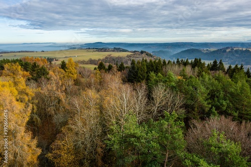 View of autumn landscape with yellow and green trees, distant hills, foggy valley, blue sky and clouds from the observation tower.