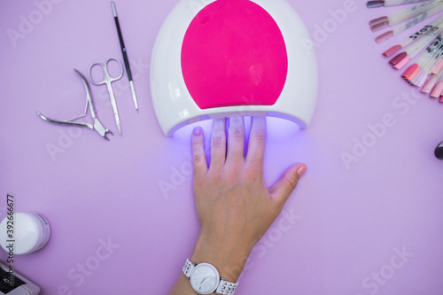 Women's hands dry gel Polish in an ultraviolet lamp, top view on the table in the salon of gel manicure. the process of drying the gel on the nails. modern manicure technology. Professional manicure 