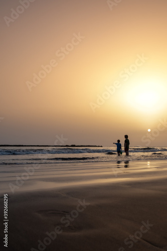 Silhouettes of two children on the beach at sunset